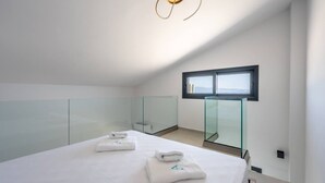 Ein modernes Schlafzimmer mit Glastrennwand, einem Bett mit Handtüchern, einem Fenster und einer außergewöhnlichen Deckenleuchte.