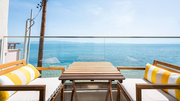 Ein Balkon mit einem Holztisch und zwei Stühlen, mit Blick auf ein Gewässer.