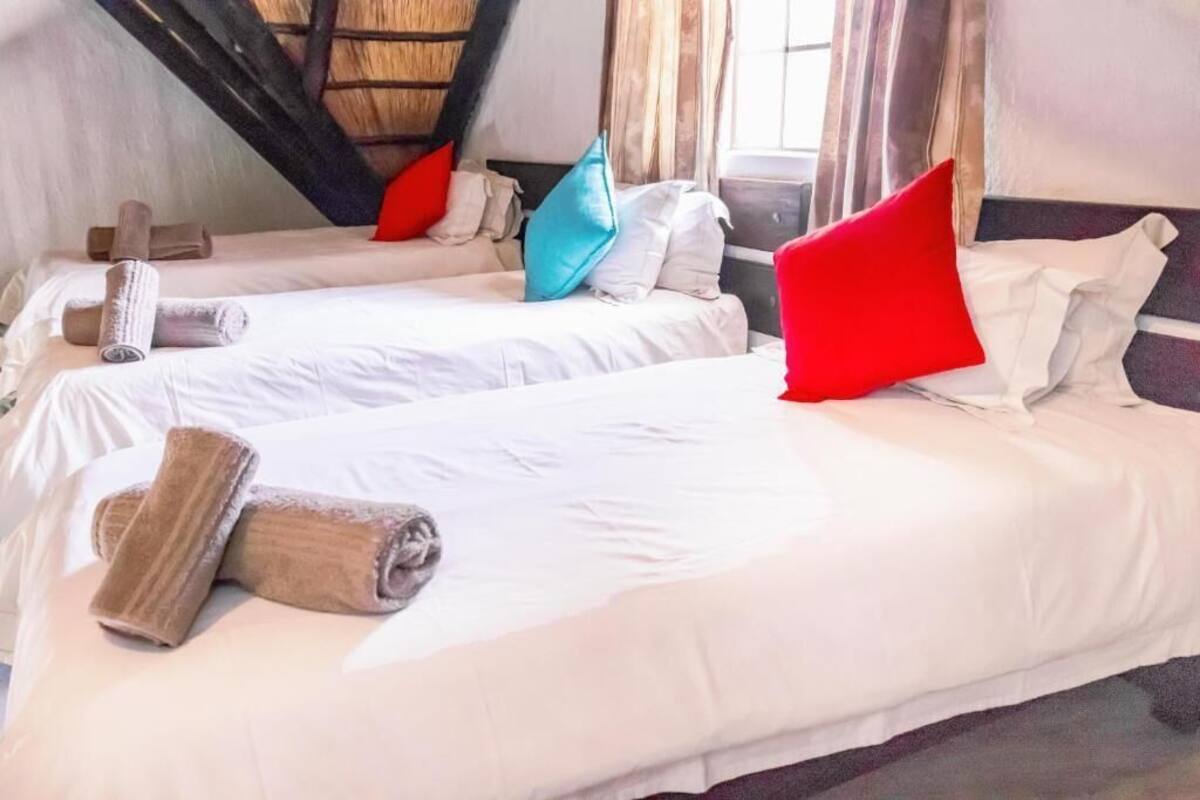 Habitación de hotel con dos camas, ropa de cama blanca y almohadas coloridas.