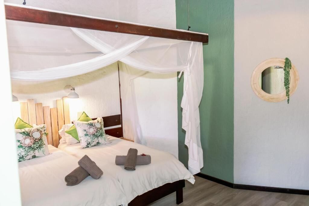 A bedroom with a canopy bed, a bedside table with a lamp, and a wall-mounted mirror.