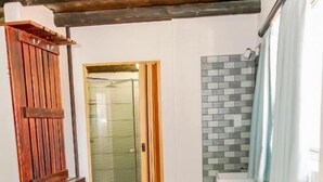 Une pièce avec une porte en bois, un banc, un mur recouvert de carreaux et une fenêtre avec des rideaux.