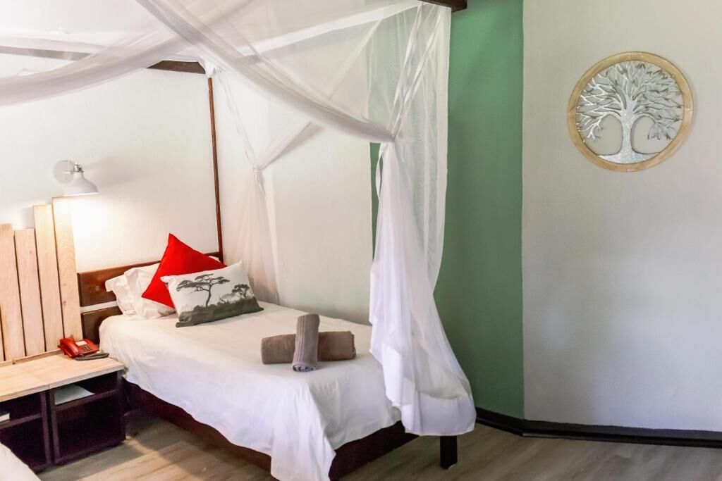 A room with a bed, a bedside table with a lamp, a wall-mounted tree decoration, and a green accent wall.