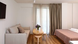 Een kamer met een bank, een bed, een klein houten tafeltje met een vaas, en een raam met gordijnen.