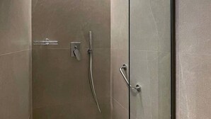 Een inloopdouche met een handdouche, bedieningspaneel aan de muur en een glazen douchedeur.