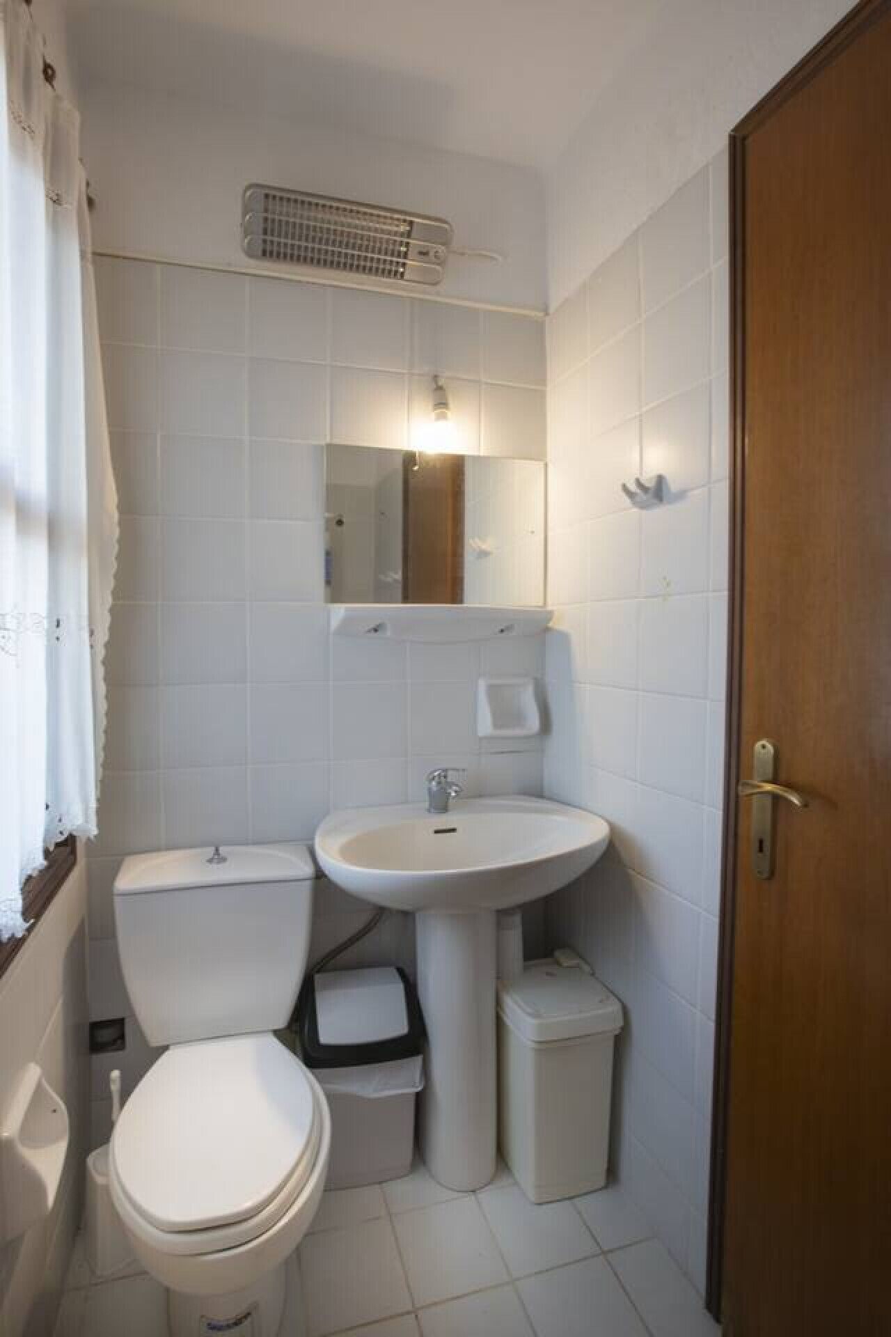 A small, compact bathroom with a toilet, sink, and mirror.