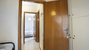 Un passadís que condueix a un dormitori amb un llit, una porta i una cadira.