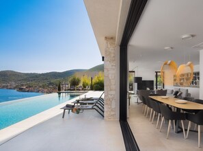 A modern hotel room with a large balcony overlooking a pool and sea, a dining area with contemporary furniture, and a view of the surrounding landscape. - Breathtaking Villa Vis (Vis)