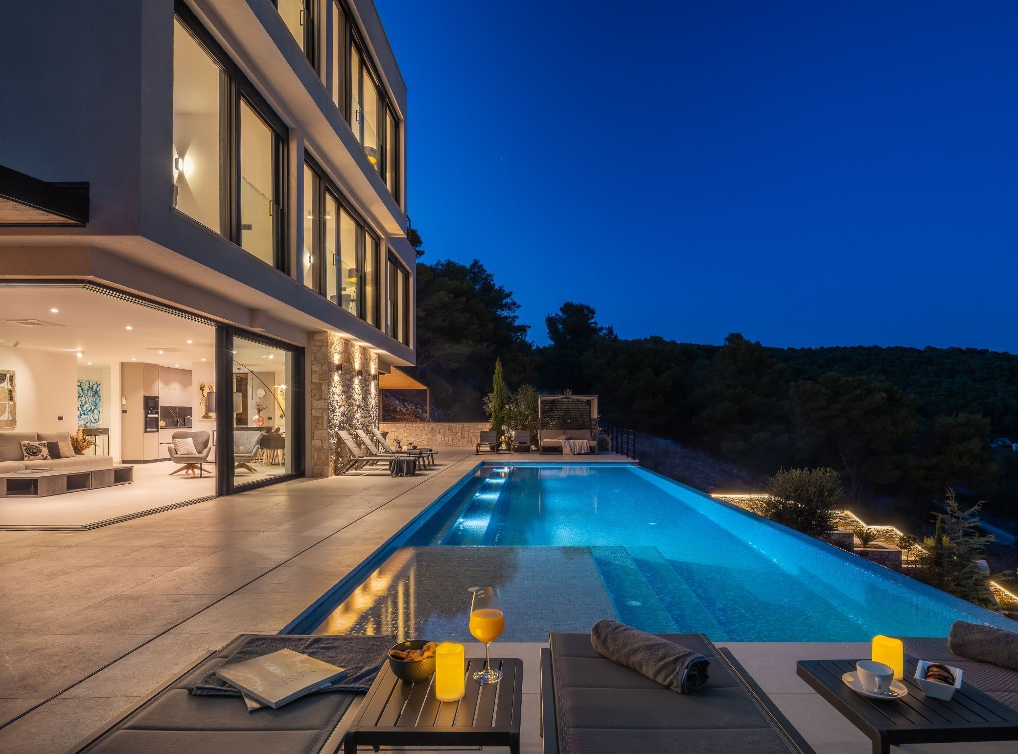 A modern house with a swimming pool, outdoor seating, and a well-lit interior.
