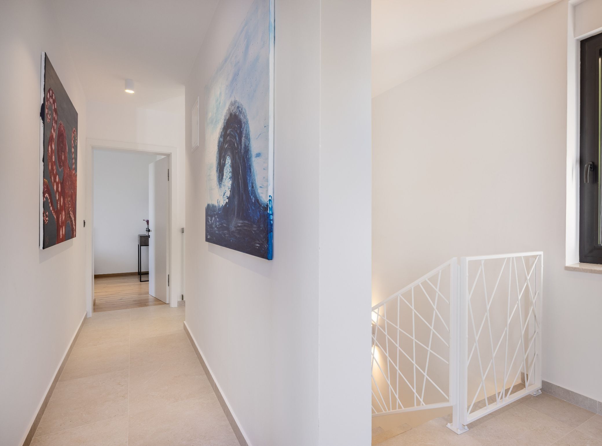 A hallway with two paintings, a door at the end, and a white railing.