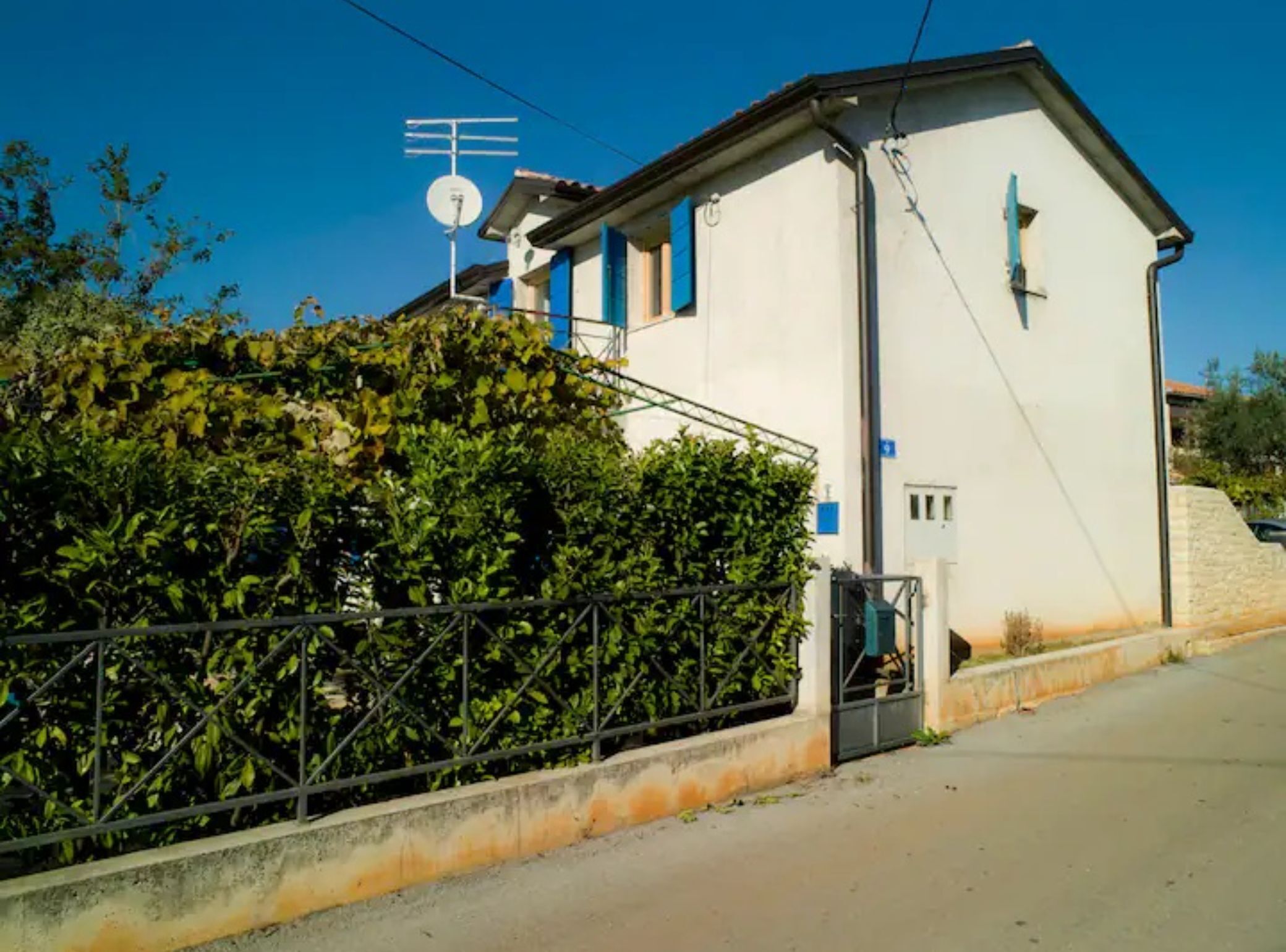 Una casa de dos pisos con antena parabólica, un pequeño porche y una cerca de metal.