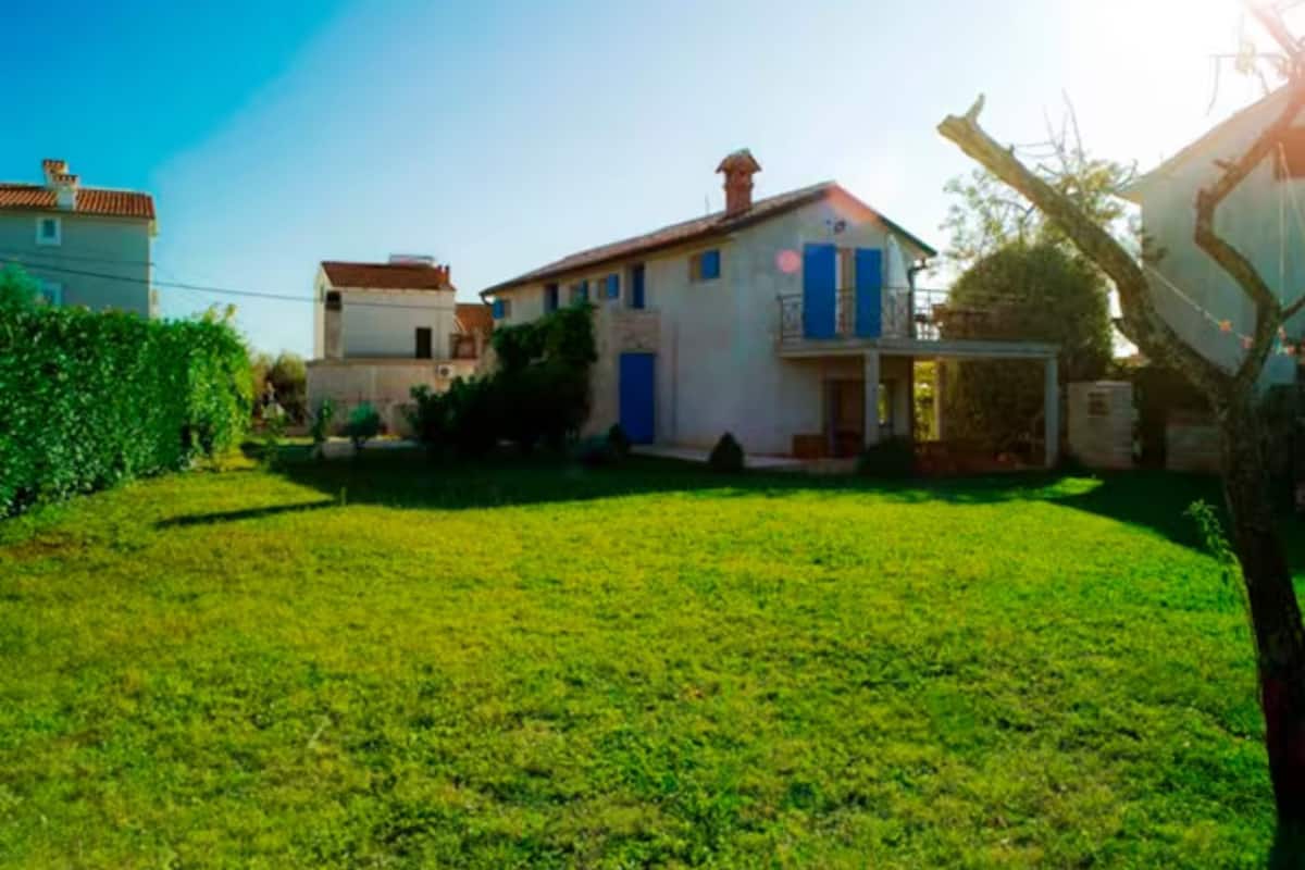 Una propiedad residencial con un césped bien cuidado, una casa de dos pisos con balcón y un garaje.