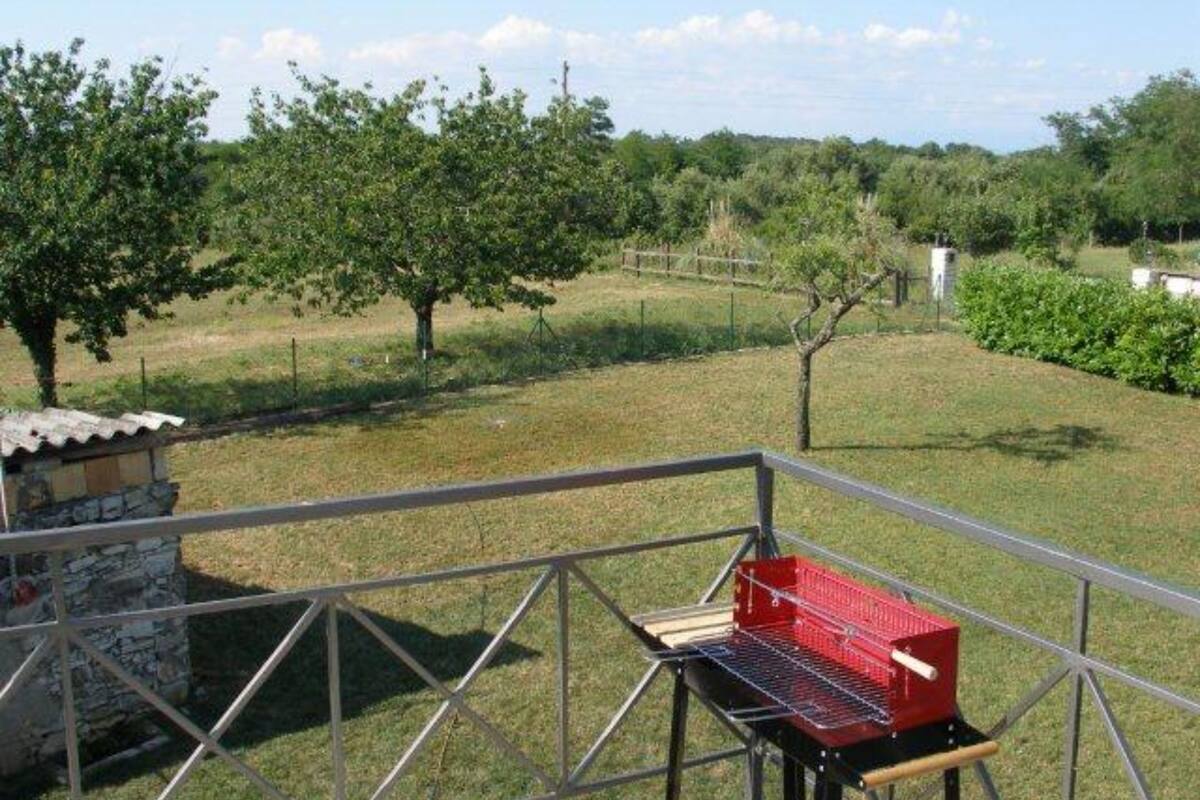 Un patio con una parrilla, una estructura de piedra y vistas a un área verde con árboles.