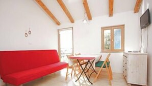 A room with a red sofa, a dining table with chairs, a window, and a TV mounted on the wall. - Authentic Istrian Apartments Villa Zambratija (Umag)