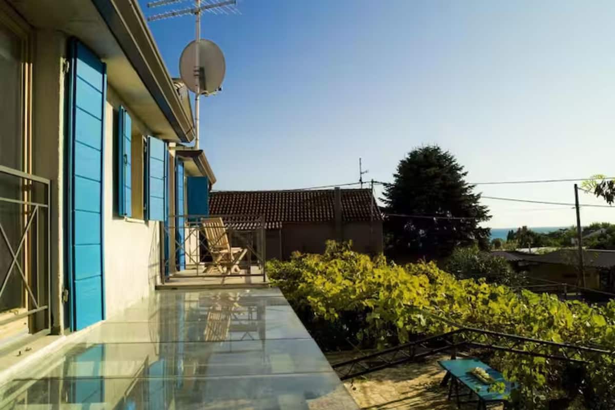 Un edificio moderno con balcón de cristal, una antena parabólica y vistas al entorno verde.