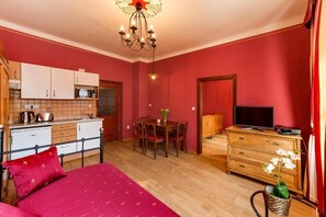 A room with a bed, a dining table, a TV, a kitchen area, and a chandelier. - Apartments Kájovská 63 - apartment 1 Red (Český Krumlov)