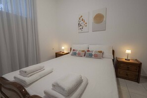 A neatly made bed with white linens and towels, two bedside tables with lamps, and two wall art pieces above the bed.