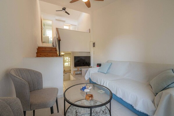 A living room with a sofa, a chair, a glass coffee table, a TV, and a ceiling fan.