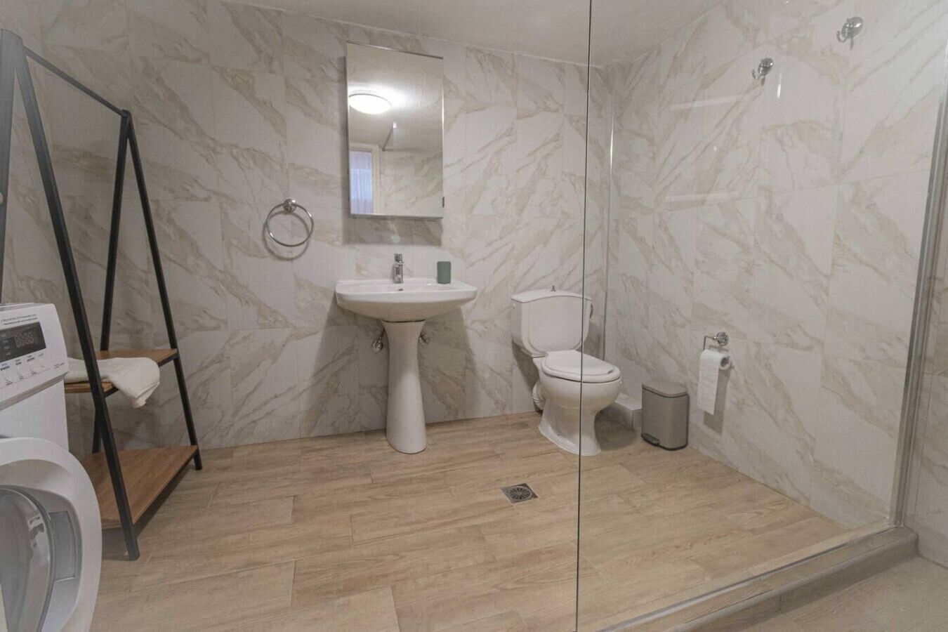 Ein Badezimmer mit Marmorwand, Waschbecken, Toilette, Dusche und Waschmaschine.