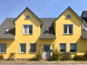 A yellow building with multiple windows and a door, surrounded by greenery.