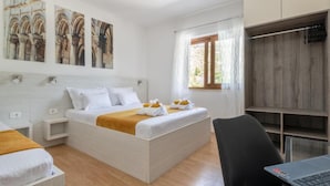 A bedroom with a bed, bedside tables, a desk with a laptop, a window with curtains, and artwork on the wall.