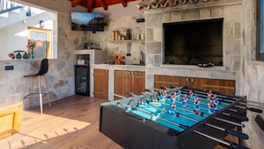 A cozy room with a foosball table, stone walls, a TV, and a stone fireplace.