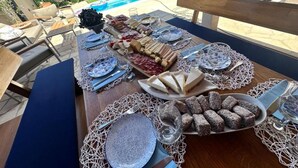 An outdoor dining area with a pool view, a table set with plates, glasses, and a variety of food.