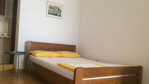 A single bed with a wooden frame and yellow bedding, a small stool, and a framed picture on the wall. - Apartments Aleksić, Bečići (Bečići)