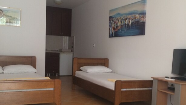 A room with two wooden beds, a small kitchenette, a television, and a painting on the wall. - Apartments Aleksić, Bečići (Bečići)