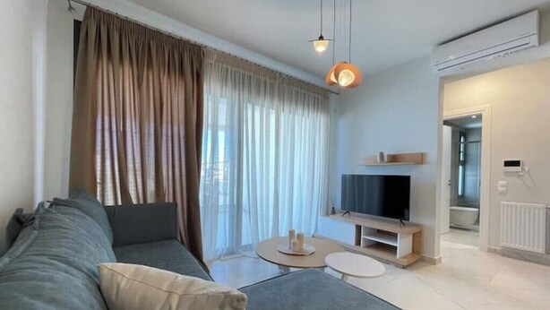 A modern living room with a sofa, TV, and a small round table. - Athenean Oasis In Ellinikon-D3 (Elliniko)