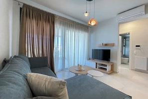 A modern living room with a sofa, TV, and a small round table. - Athenean Oasis In Ellinikon-D3 (Elliniko)
