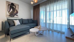 A modern living room with a grey sofa, a round coffee table, and a painting on the wall. - Athenean Oasis In Ellinikon-D3 (Elliniko)