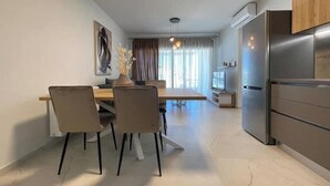 A modern kitchen with a stainless steel refrigerator, a dining area with a table and chairs, and a large window with curtains. - Athenean Oasis In Ellinikon-D3 (Elliniko)
