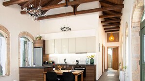 Una cocina moderna con vigas de madera, un área de comedor con mesa y sillas, y un pasillo que conduce a una puerta.