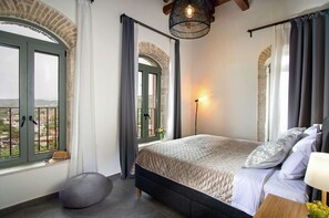 A bedroom with a bed, a lamp, a window with curtains, and a view of the outside. - Vineyard View, next to Best Wineries, "Trigos" appartment (52QJ+W6 Avgeniki)