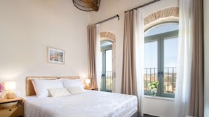 Un dormitorio con cama, mesitas de noche, lámpara, un cuadro en la pared y ventana con cortinas.