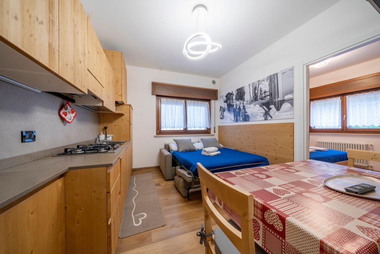 A compact room with a kitchenette, a bed, a dining table, and a window with curtains.