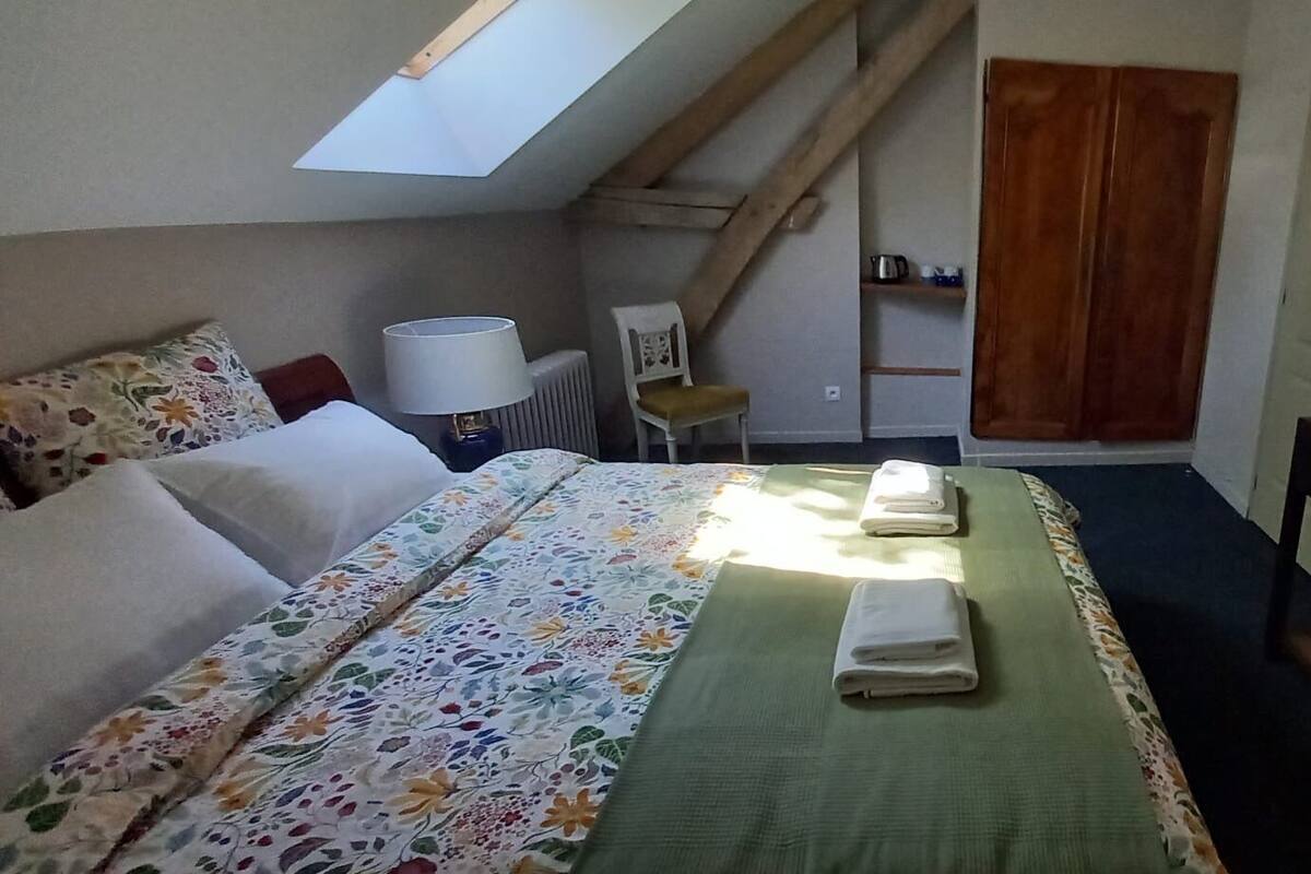 Een slaapkamer met een bed, een bureau, een stoel, een radiator, een plankje met toiletartikelen, een houten deur en een dakraam.