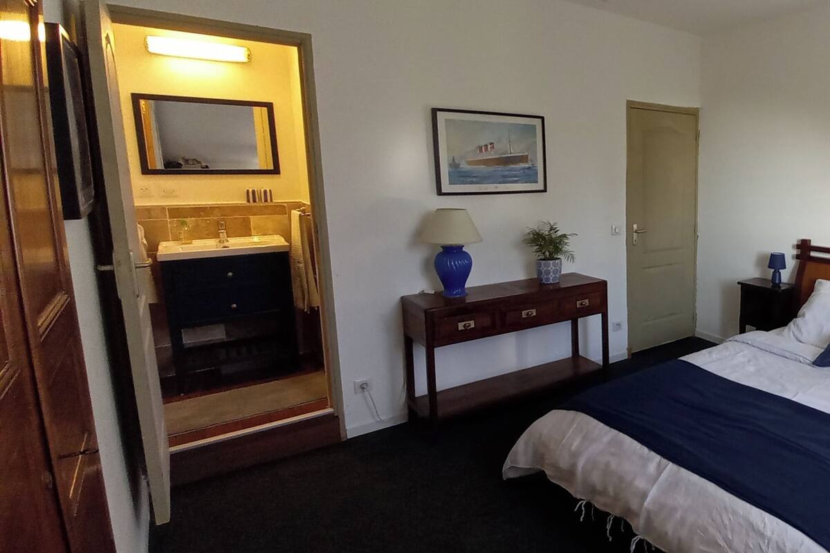 Een slaapkamer met een bed, nachtkastje, lamp en een schilderij aan de muur.