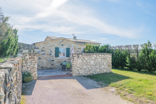 Un bâtiment en pierre avec une entrée pavée, un petit espace extérieur aménagé avec des sièges et un mur en pierre.