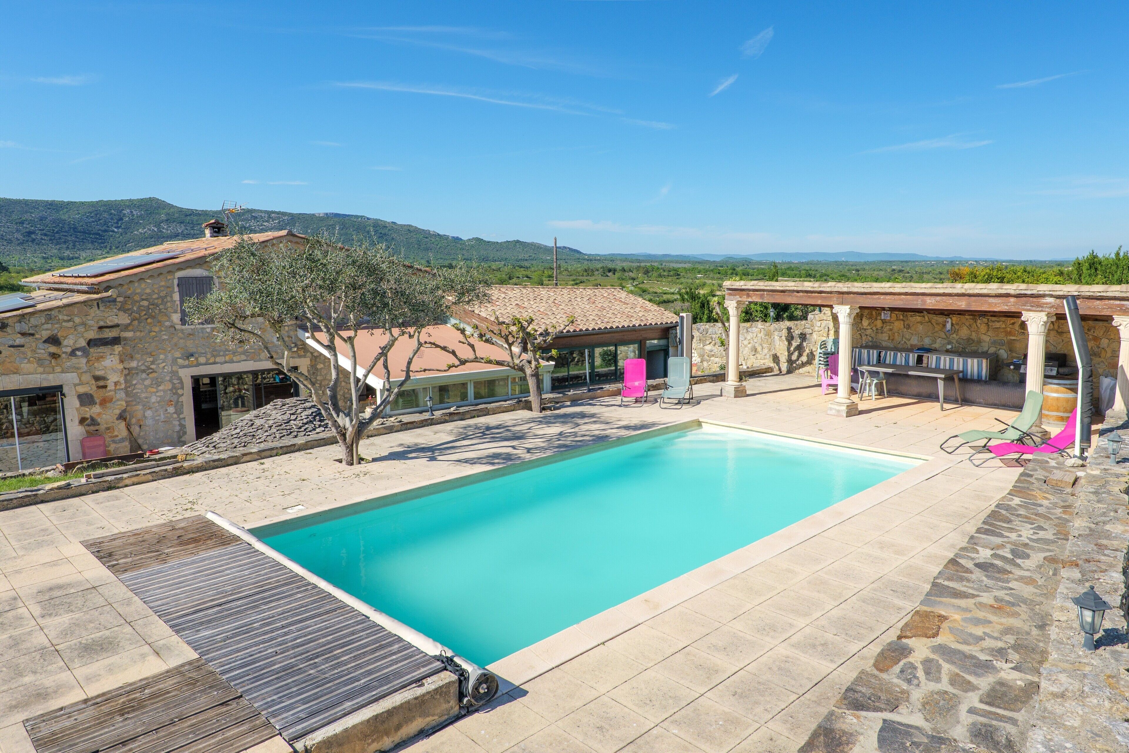A swimming pool with a stone deck, a covered patio area, and a view of the surrounding landscape.