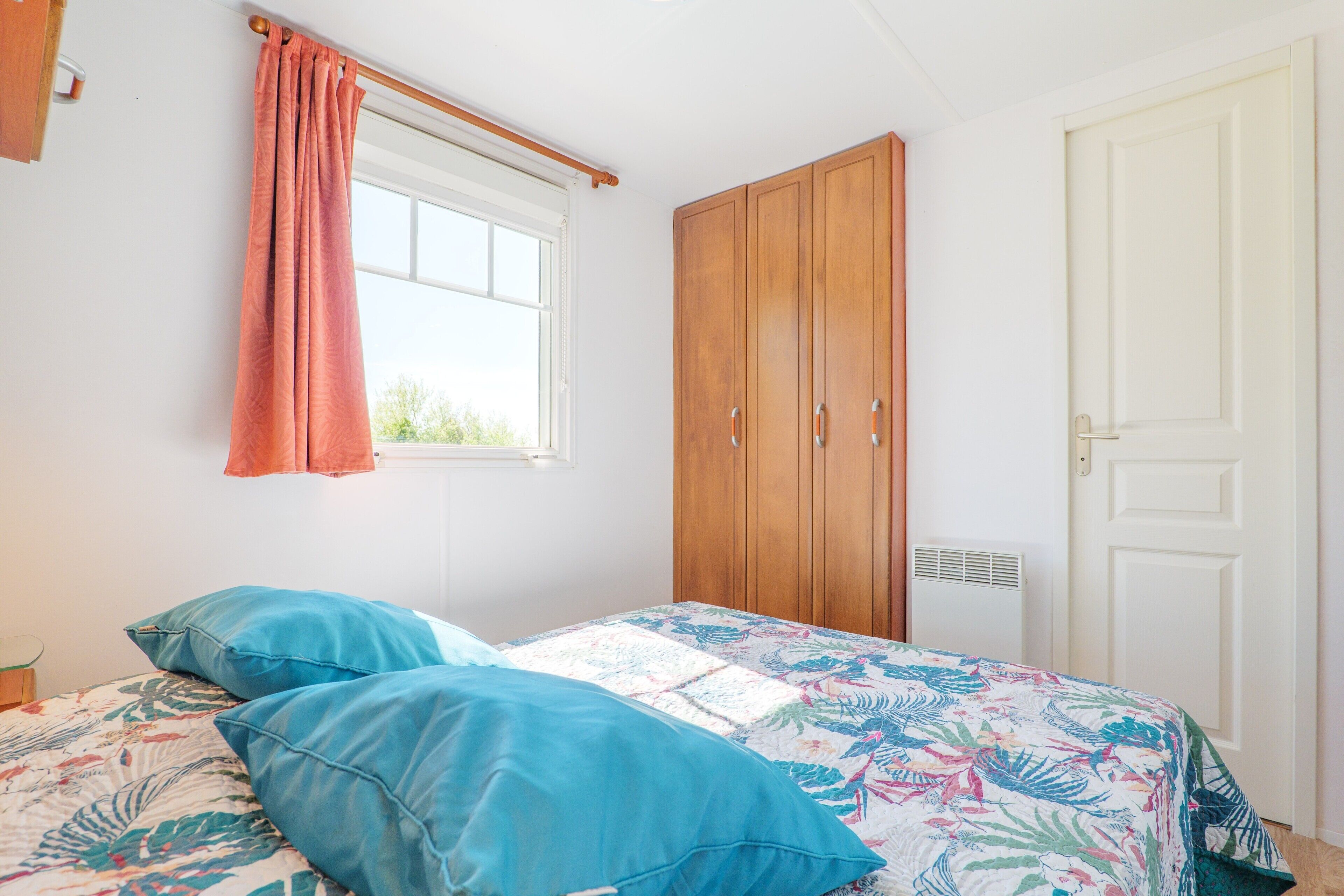 A bedroom with a bed, a window with curtains, a wardrobe, and a door.