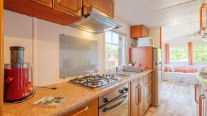 A compact kitchen with a gas stove, oven, and microwave, wooden cabinets, and a window providing natural light. - Charming Bungalow with Private Pool, Wi-Fi, and Air Conditioning (Saint-Remèze)