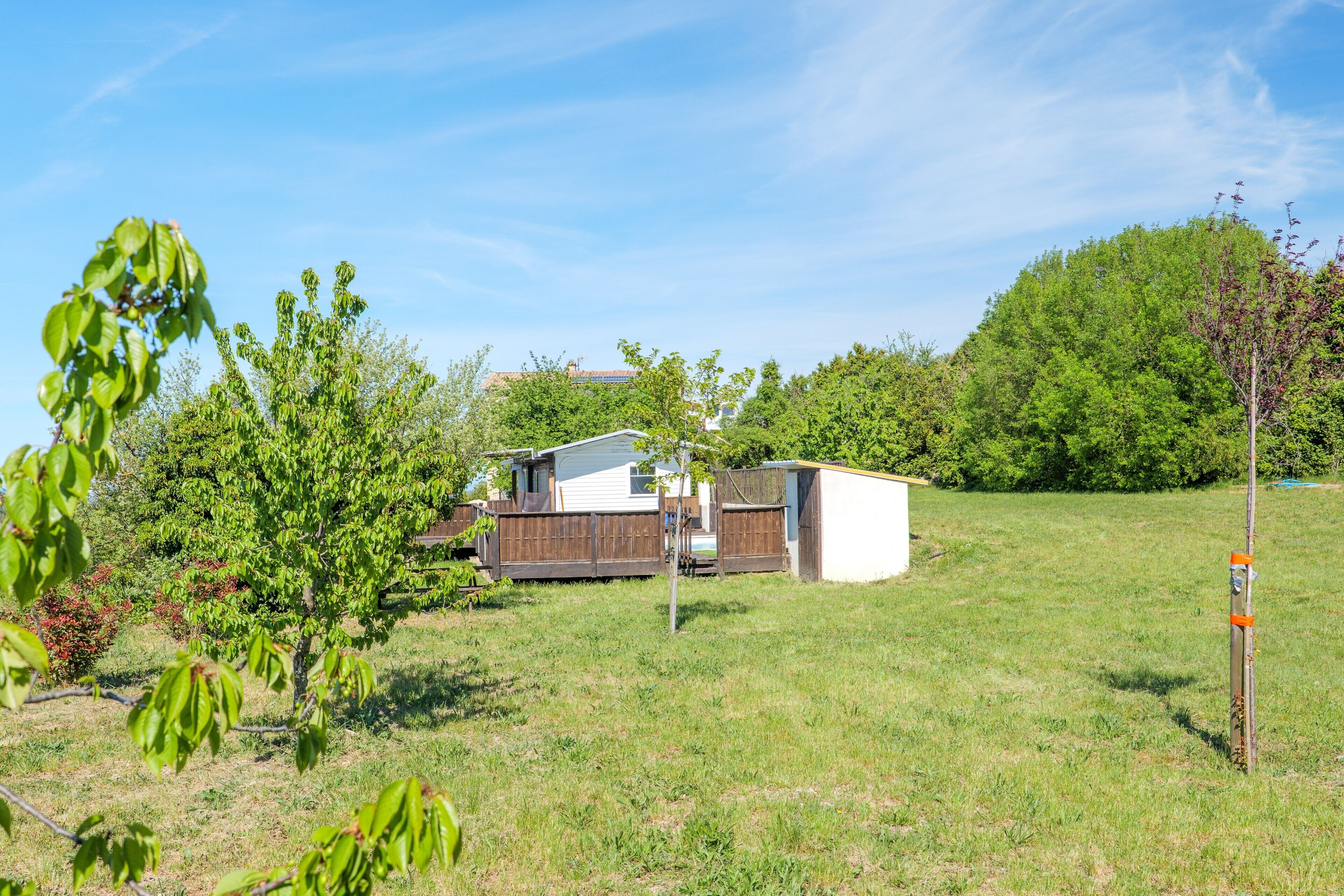 Un quartier résidentiel avec une maison blanche, une terrasse en bois et une cour clôturée.