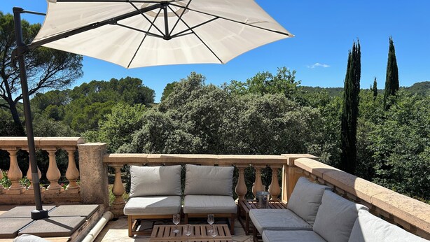 Un espace extérieur aménagé avec une balustrade en pierre, des canapés confortables, une table en bois et un grand parasol.