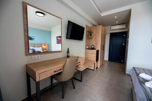 A modern hotel room with a wooden desk, a chair, a bed, a TV, and a wardrobe. - Calda Resort (Polygyros)