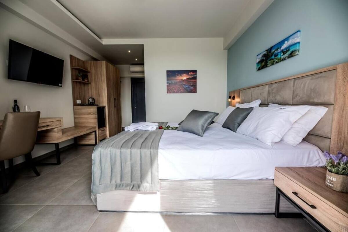 A modern hotel room with a large bed, a TV mounted on the wall, a desk, and a painting.