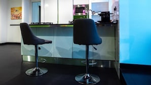 Una cucina moderna con angolo bar, caratterizzata da elettrodomestici in acciaio inox, due sgabelli da bar e illuminazione a sospensione.