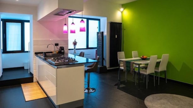 Una cucina moderna con isola centrale, zona pranzo con sedie e una parete verde a contrasto.