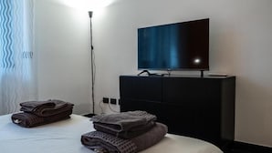 Camera d'albergo con un letto, una TV a schermo piatto montata su un mobile nero e una lampada da terra.