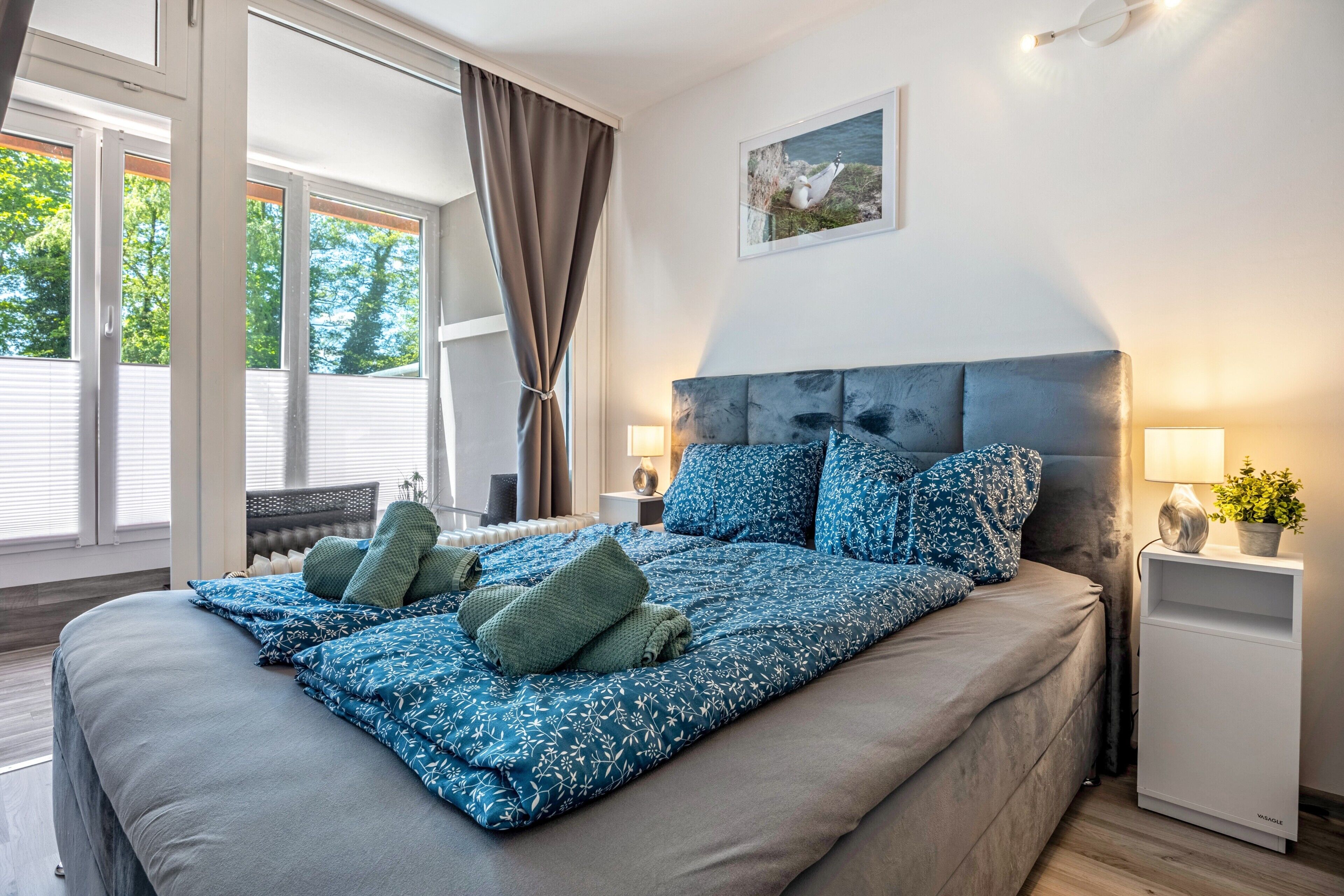 Een slaapkamer met een groot bed, een hoofdbord, nachtkastje, lamp en een raam met gordijnen.